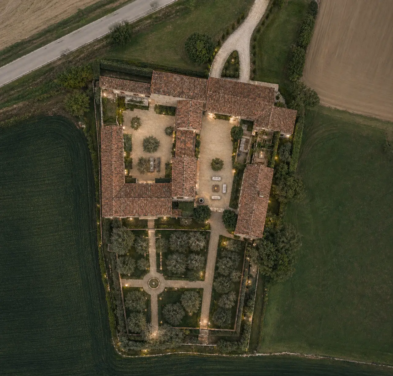 Aerial view of a restored walled estate with formal gardens and tiled roofs at dusk
