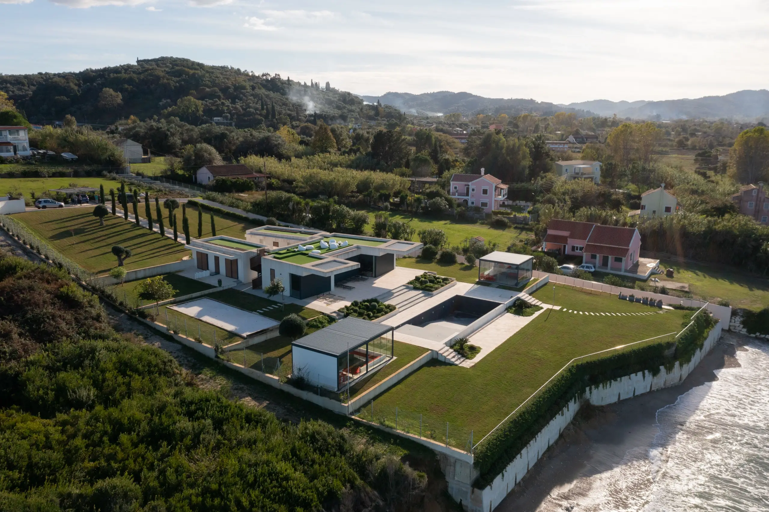 Aerial view of a modern coastal villa set within manicured gardens by the sea