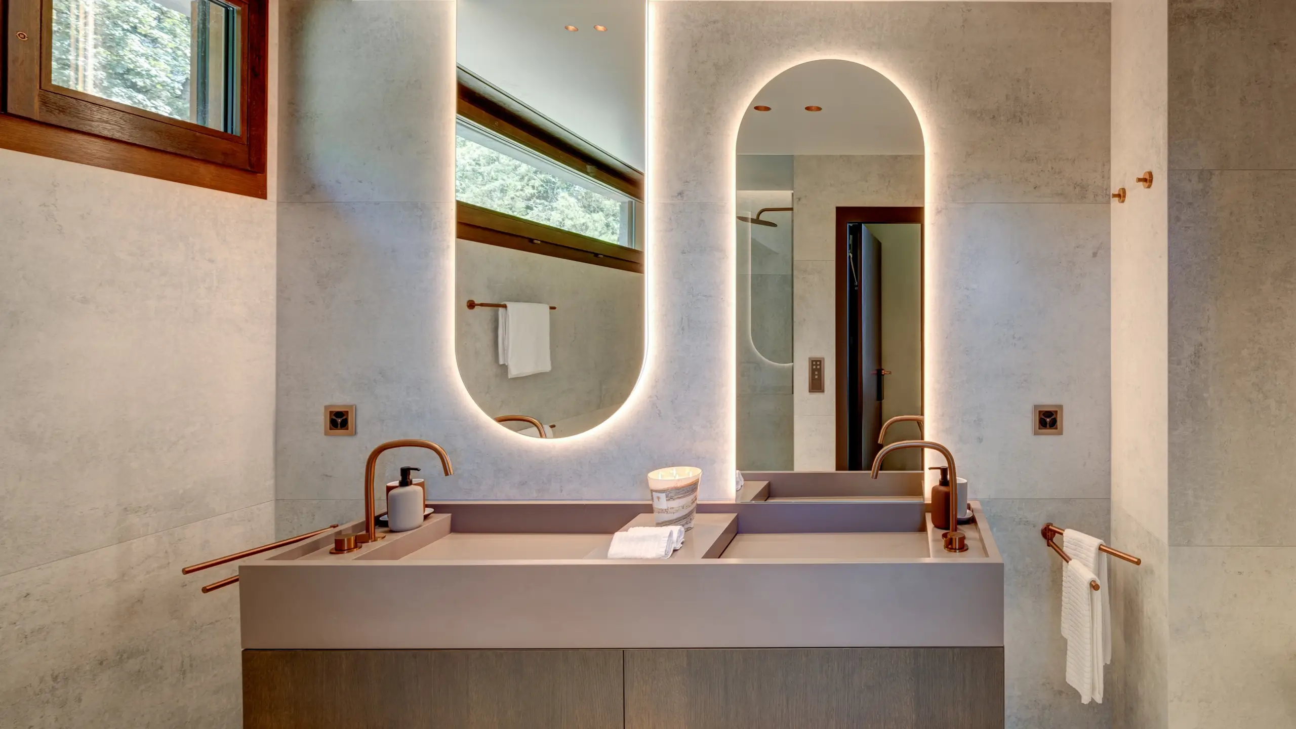 Bathroom vanity with twin backlit arched mirrors, copper fixtures and a stone counter