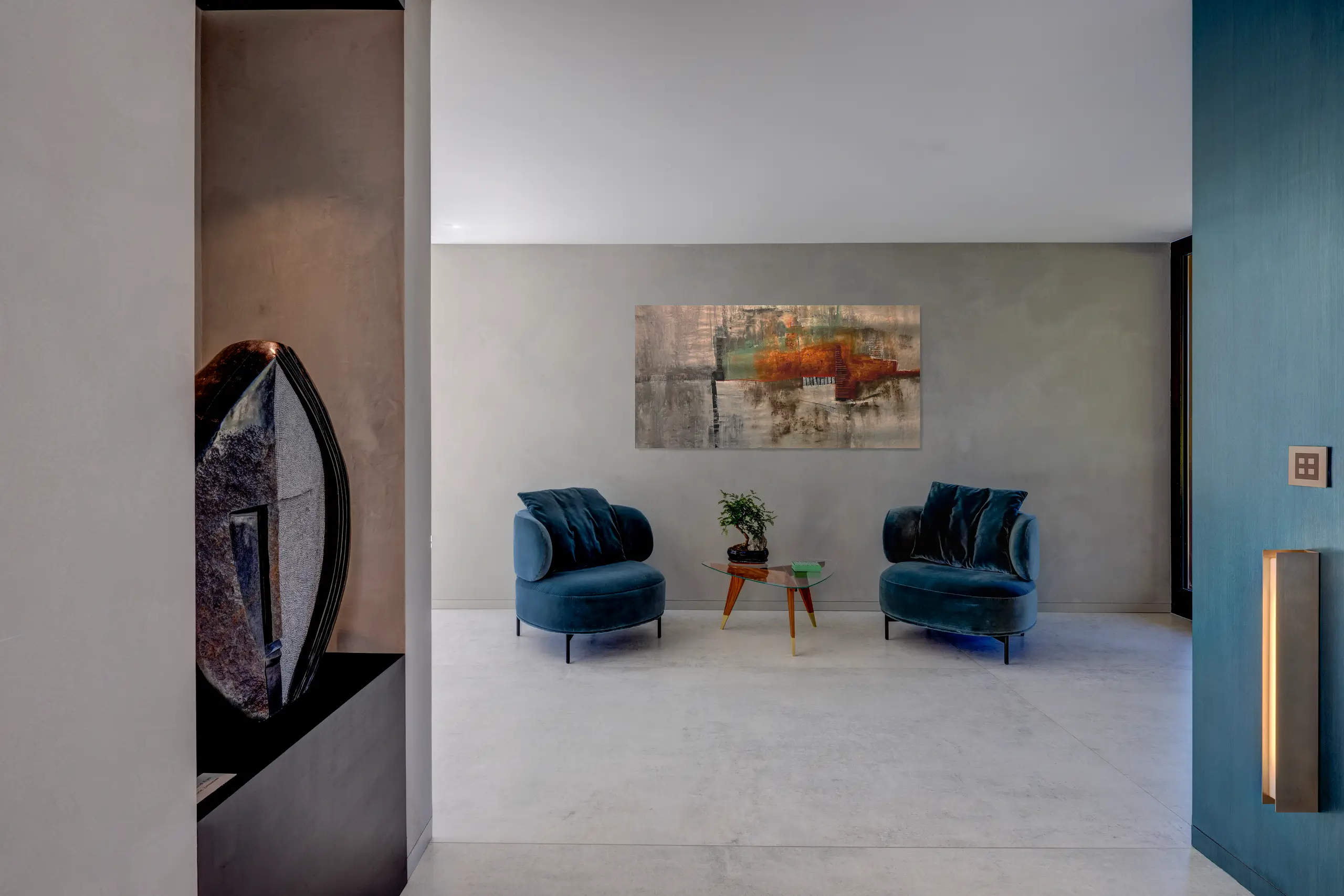 Living room with two deep blue upholstered armchairs flanking a low table beneath framed artwork