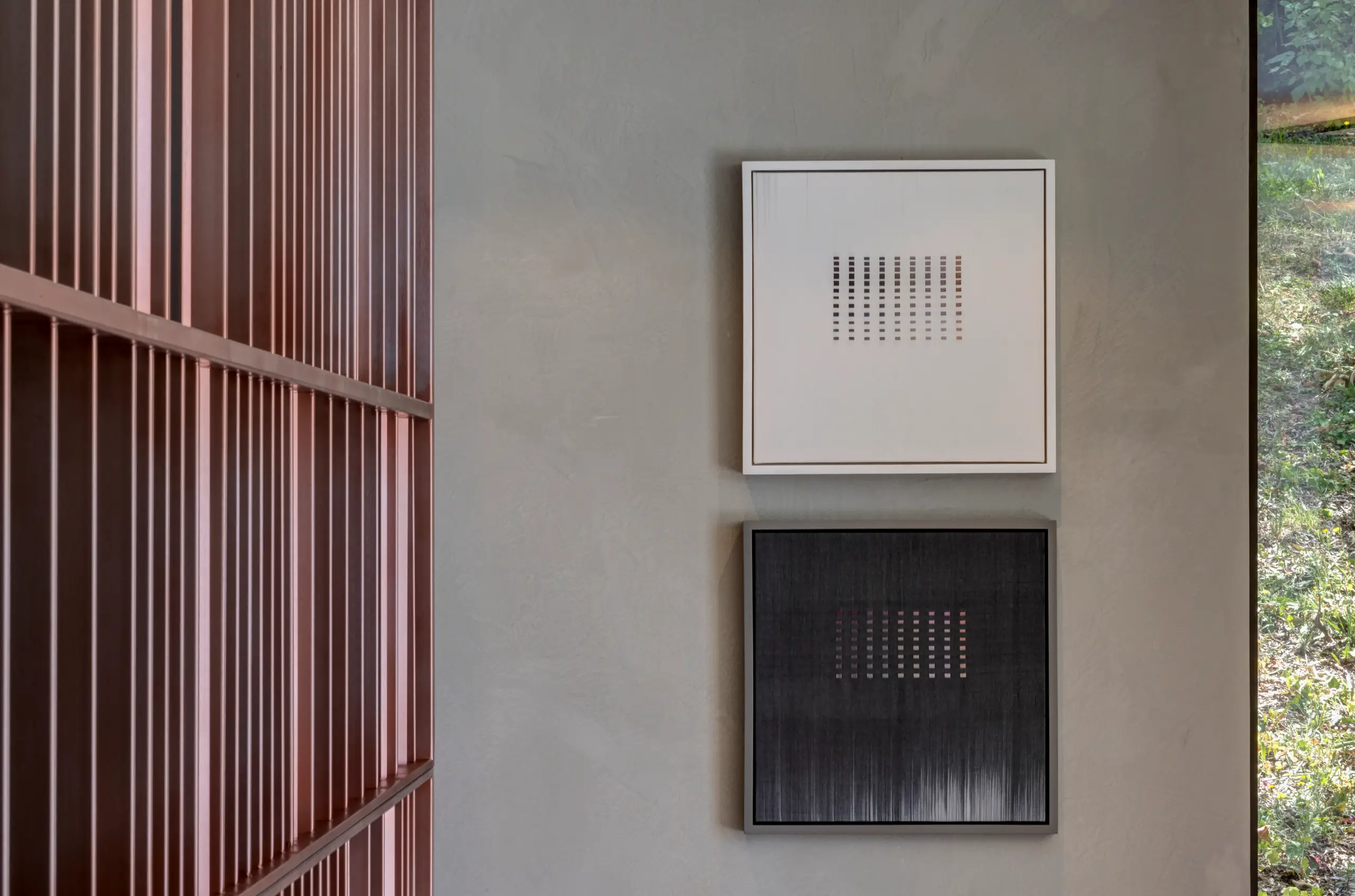 Two square framed grid artworks — one cream, one black — mounted on a pale wall