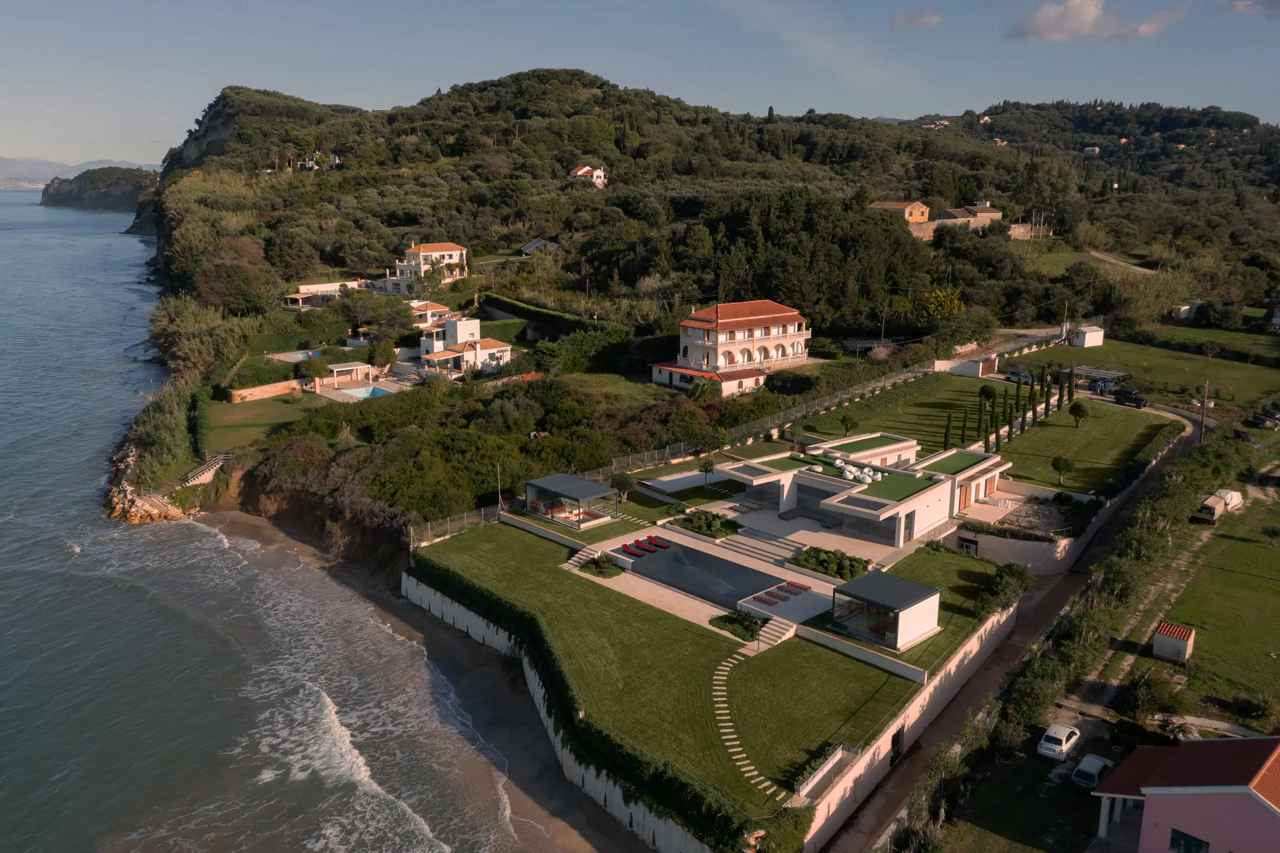 Aerial view of the estate poised on a clifftop above a sandy cove, the new pavilions sitting beside an older villa overlooking the Ionian Sea