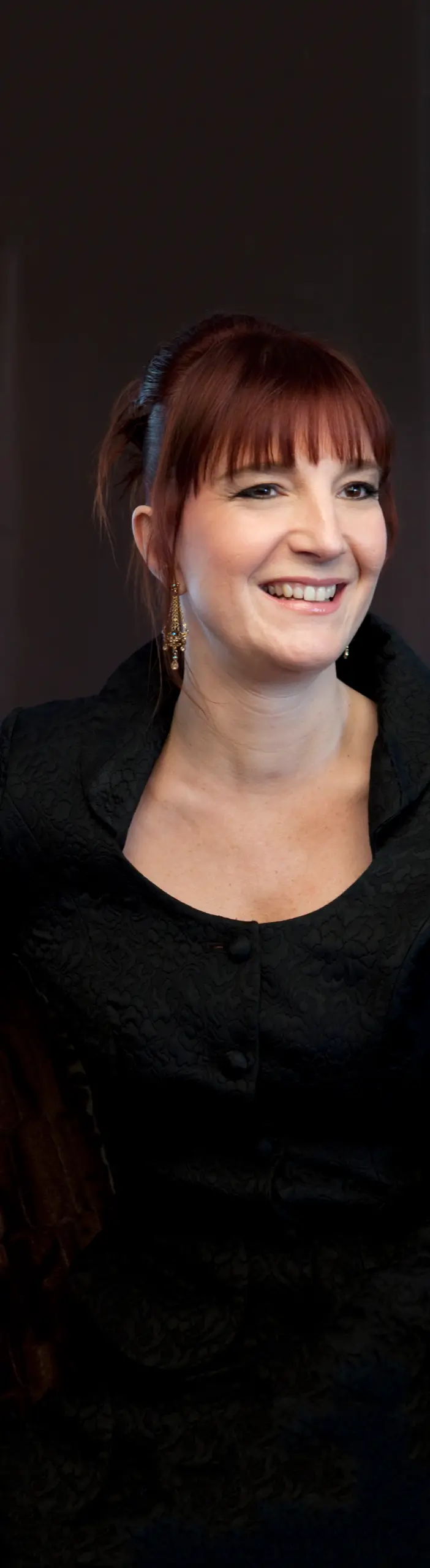 Milena Cvijanovich, seated in black against a dark backdrop, smiling