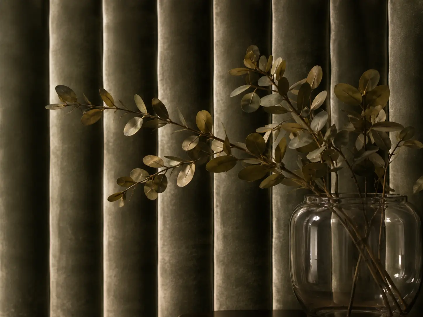 Pleated velvet curtain behind a glass vase of dried leaves