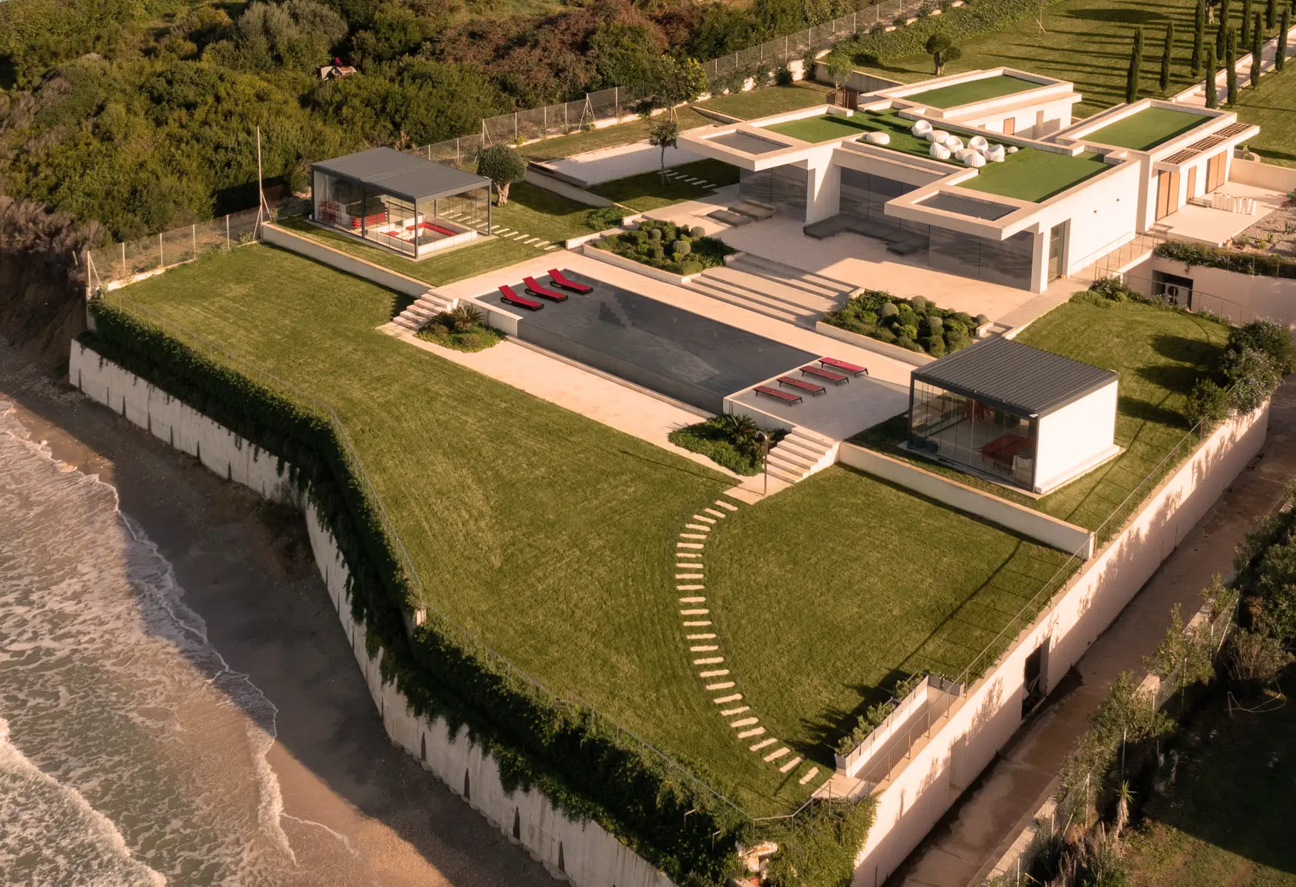 Aerial view of a modern coastal villa set within manicured gardens by the sea